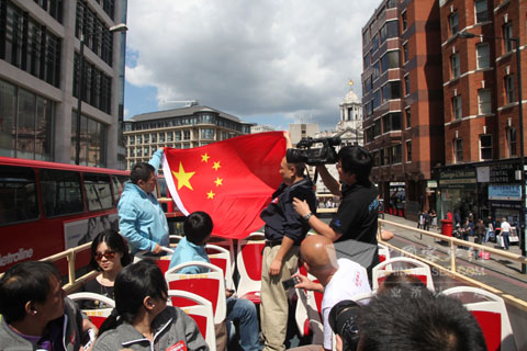 中國(guó)游客們?cè)诎矂P雙層車上揚(yáng)起國(guó)旗為奧運(yùn)健兒助威